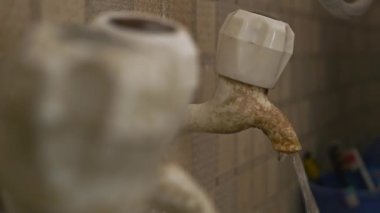 Su, bir banyonun içindeki eski kirli bir plastik musluktan akıyor.