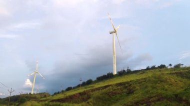 Hindistan köylerinin dışında günbatımında dağın tepesinde dönen rüzgar türbinlerinin görüntüsü.