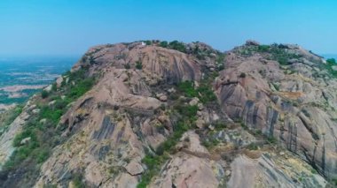 Hindistan 'da yaz boyunca büyük bir kaya dağının kıyısındaki eski küçük bir tapınağın havadan görünüşü.