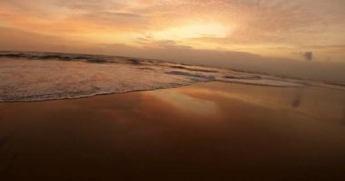 Gün batımında turuncu renkli güzel bir sahil manzarası ve yaz zamanı sakin dalgalar.