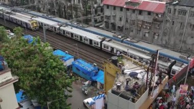 Mumbai, Hindistan-11 Eylül 2022: Kirli, eski apartmanlar arasında hızla hareket eden üç trenin hava görüntüsü