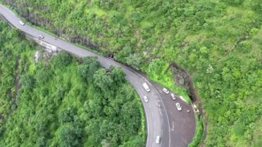 Güneşli bir günde virajlı dağ yolunda yavaşça ilerleyen trafik ve araçların hava görüntüsü