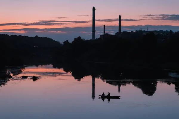 夕阳西下 两个男人坐在船上 船桨挂在工厂管子的后面 — 图库照片