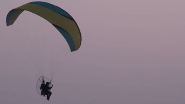 Motorlu bir paraglider akşam gökyüzünde uçuyor.
