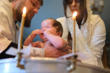 Zhytomyr, Ukrayna - 12 Eylül 2021: Kutsal suda yeni doğan bebek vaftiz töreni. Suda yıkanan bebek. Yazı tipinde vaftiz. Vaftiz ayini. Çocuk ve Tanrı. Vaftiz mumu Kutsal su yazı tipi.