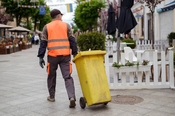 Sarı çöp kutusuyla turuncu üniformalı bir sokak çalışanı..