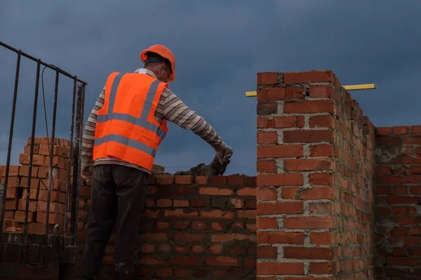 Zhytomyr, Ukrayna - 1 Ekim 2020: İşçi dramatik gökyüzü arka planında inşaat sahasına tuğla döşedi.