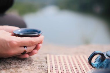Mavi bardağı elinde çayıyla tutan bir kız. Kayalarda çay seremonisi. Doğada arkadaşlarla vakit geçirmenin yolu.