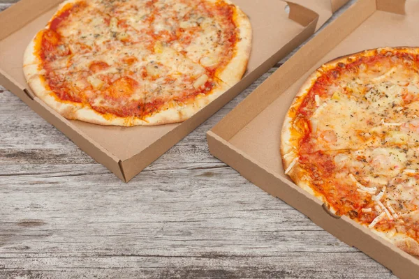 two pizzas at paper boxes. Top view of fresh baked pizza with meat and vegetables on wooden table. food delivery and take away.