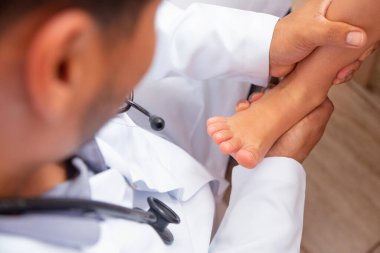 Hastanede çocukların ayaklarını muayene eden bir doktor. Cerrah, travmatolog ya da ortopedi uzmanı kızın bacağını ve ayağını elliyor.