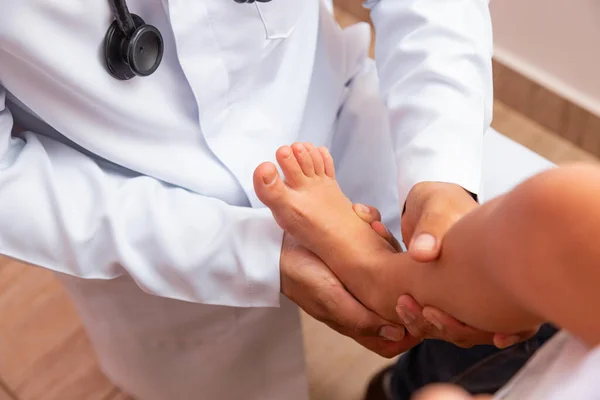 doctor examining children's feet in hospital. Surgeon, traumatologist or orthopedist palpating girl's leg and foot