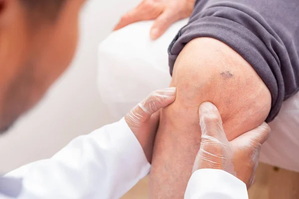 physiotherapist doctor examining, massaging and treating elderly patient knee and leg in orthopedic medical clinic nursing hospital.
