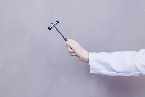 The doctor is holding a neurological hammer on a grey background. The neurologist checks the patient's reflexes with a hammer. Diagnostics, healthcare, and medical care