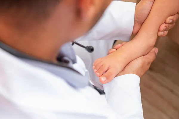 doctor examining children's feet in hospital. Surgeon, traumatologist or orthopedist palpating girl's leg and foot