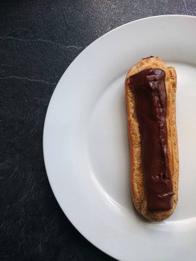 Eclair au chocolat sur une assiette blanche pos sur un fond gris