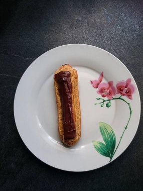 Eclair vu de haut sur une assiette blanche avec une orchide dessin et un fond gris