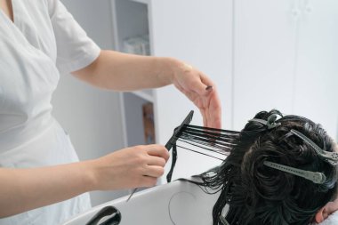 Güzellik uzmanı maske takıyor. Saçında ve hastanın siyah saçlarını tarıyor. Artı boyut. beyaz dolap