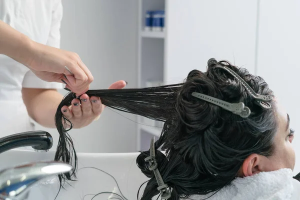 Güzellik uzmanı maske takıyor. Saçında ve hastanın siyah saçlarını tarıyor. Artı boyut. beyaz dolap