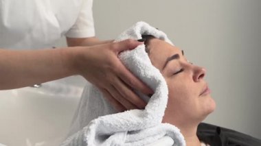 Güzellik uzmanı, müşteriye havlu ile kafasını kurutur. lavabo, siyah saç, artı beden.