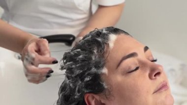 Kozmetik uzmanı ameliyatlar için kızın kafasını şampuanla yıkar. Siyah saçlı. artı boyut.