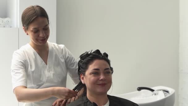 美容师戴上面具 在她的头发上梳理病人的黑头发 加尺寸白色橱柜 — 图库视频影像