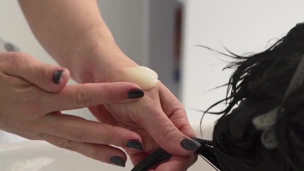 美容师戴上面具 在她的头发上梳理病人的黑头发 加尺寸白色橱柜 — 图库视频影像