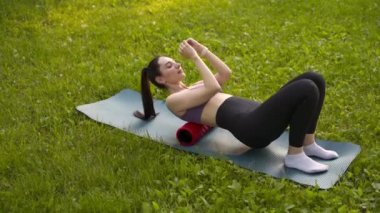 Parktaki bir kız spor için arka planda mavi bir spor paspasın üzerinde mor bir bluzla spor yapmaya gidiyor. Bir çayır ve ağaçlar.