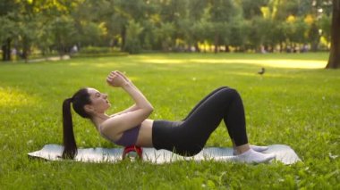 Parktaki bir kız spor için arka planda mavi bir spor paspasın üzerinde mor bir bluzla spor yapmaya gidiyor. Bir çayır ve ağaçlar.