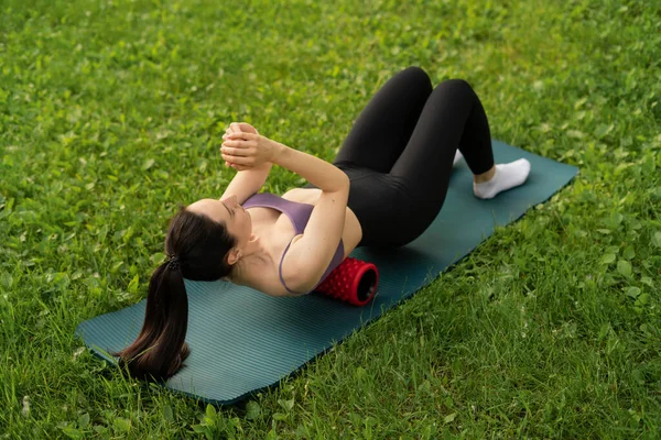 Parktaki bir kız spor için arka planda mavi bir spor paspasın üzerinde mor bir bluzla spor yapmaya gidiyor. Bir çayır ve ağaçlar.