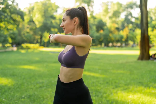 Parktaki bir kız spor için arka planda mavi bir spor paspasın üzerinde mor bir bluzla spor yapmaya gidiyor. Bir çayır ve ağaçlar.