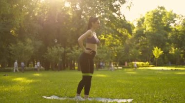 Parktaki bir kız spor için arka planda mavi bir spor paspasın üzerinde mor bir bluzla spor yapmaya gidiyor. Bir çayır ve ağaçlar.