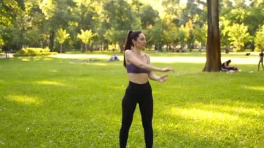 Parktaki bir kız spor için arka planda mavi bir spor paspasın üzerinde mor bir bluzla spor yapmaya gidiyor. Bir çayır ve ağaçlar.