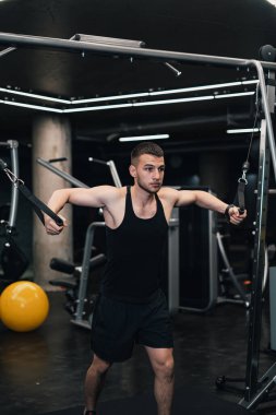 Adam göğsünü spor salonundaki simülatöre pompalıyor. koyu arkaplan