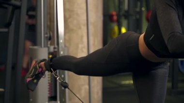 Kız sporcu spor salonundaki simülatörde bacaklarını sallıyor. koyu arkaplan