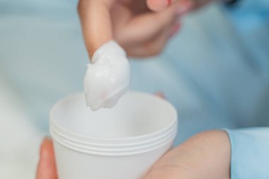 Kız kavanozdan beyaz kremayı yakın plan çekerek çıkarıyor.