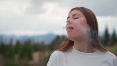 Kız, arka plandaki dağlarda elektronik sigara içiyor.