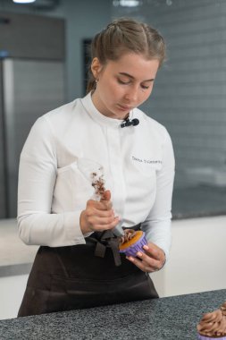 Kız keklerin üzerine krema sıkıyor.