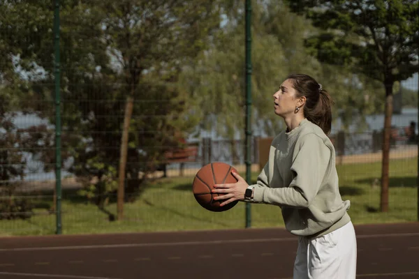 Kız basketbol sahasında topu ringe atıyor.