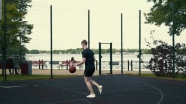 Adam basketbol sahasında topu ringe fırlatıyor.