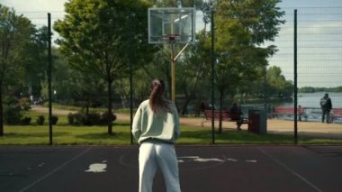 Kız basketbol sahasında topu ringe atıyor.