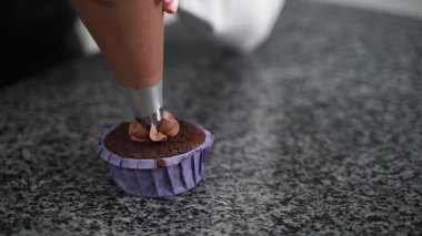 Şef mor ambalajlı kahverengi keke kahverengi krema sürüyor.