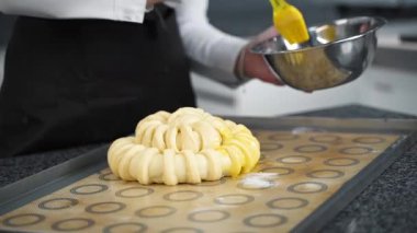 Şef turta yapmak için çiğ pesto üzerine yumurta sarısı fırçalıyor.