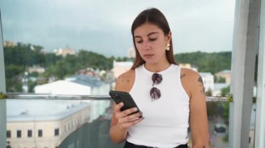 Bir kız Kyiv 'in ortasında dönme dolaba biniyor ve telefona bakıyor.