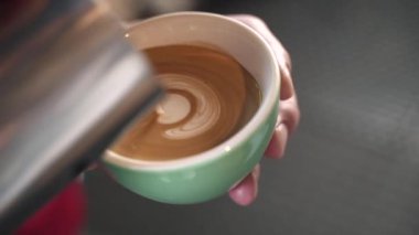 Kırmızı tişörtlü barista yeşil bardağa kahve doldurur.