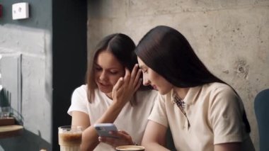 Kızlar bir kafede oturup kahve içerler ve telefona bakarlar.