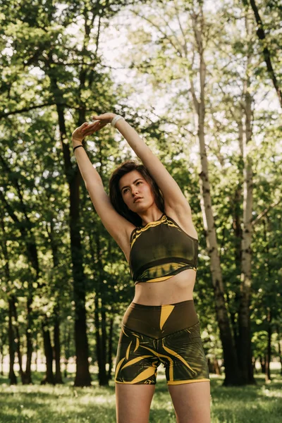 a young girl goes in for sports in the park / in the forest. in a green suit on a yoga mat