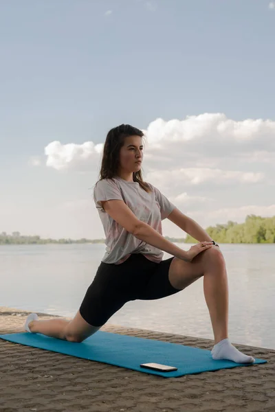 Genç bir kız yoga yapıyor. Akşamları nehrin kıyısında yoga minderinde.