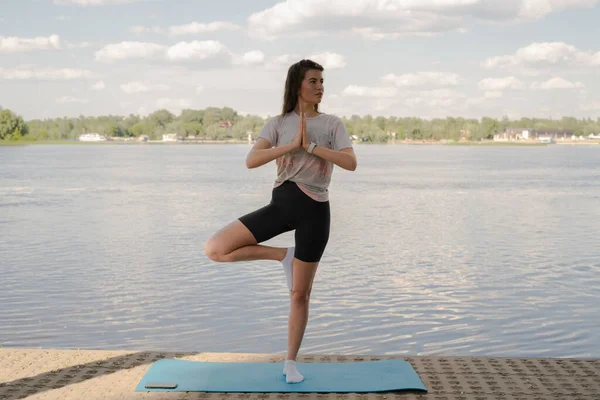 Genç bir kız yoga yapıyor. Akşamları nehrin kıyısında yoga minderinde.