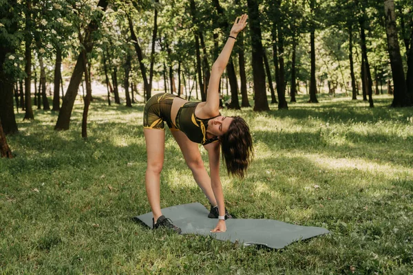 a young girl goes in for sports in the park / in the forest. in a green suit on a yoga mat