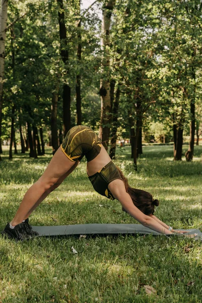 a young girl goes in for sports in the park / in the forest. in a green suit on a yoga mat